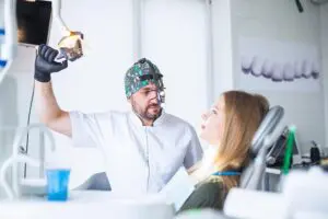 Image URL: https://pixabay.com/photos/preventive-dentistry-dentistry-8858477/ ALTText: Woman sitting in a dentist chair with a dentist next to her getting ready for an exam. 