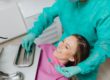 Woman sitting back in a dental chair. The dentist is holding and exam mirror near her face