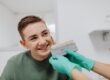 Photo by www.kaboompics.com: https://www.pexels.com/photo/a-boy-smiling-while-a-person-wearing-latex-gloves-is-holding-a-dental-shade-guide-6627273/ young man comparing tooth brightness with dentist